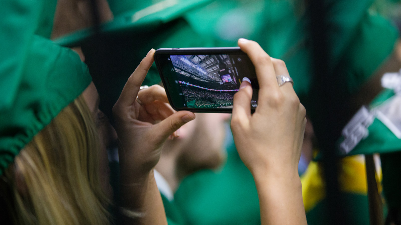 Graduating student holding up phone to take photo inside Breslin Center at commencement